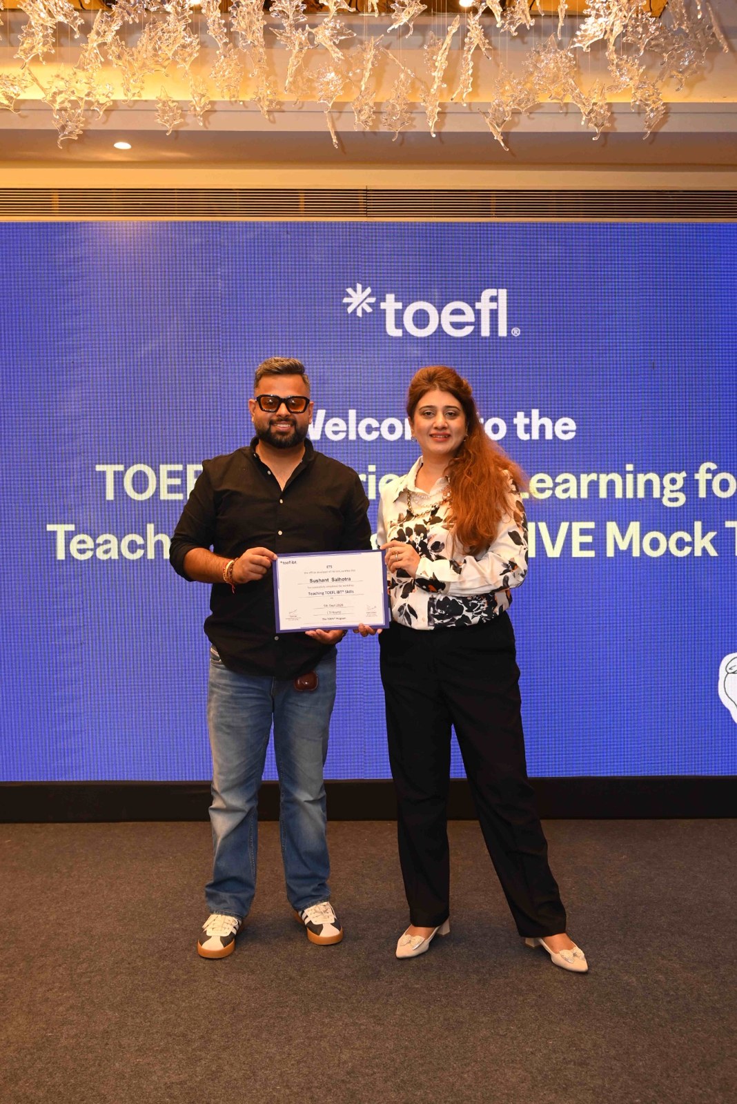 Two attendees holding a framed output on the TOEFL branded stage